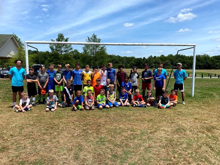 Youth soccer team posing in front of goal on grass field with trees in background