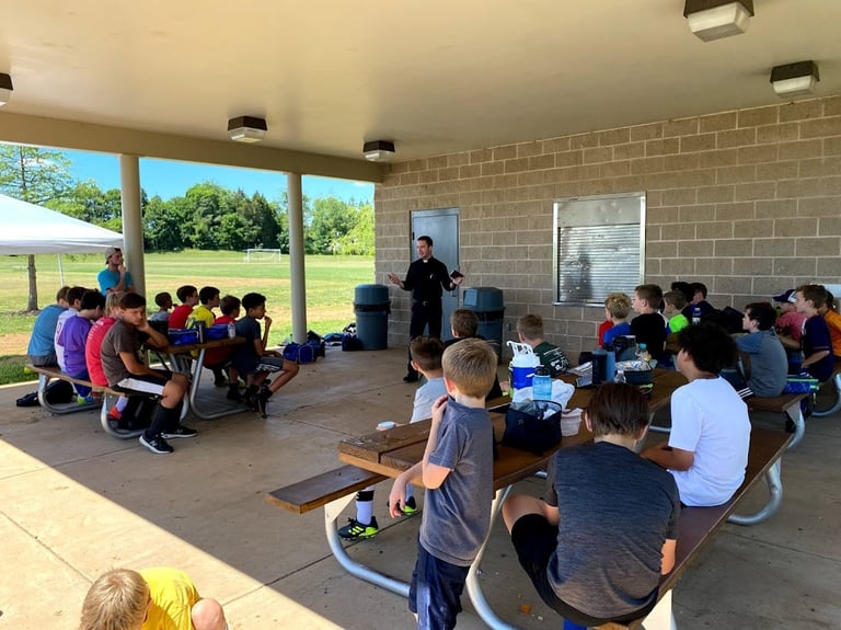 Group of children sitting on a covered patio listening to an adult presenter during an outdoor educational activity